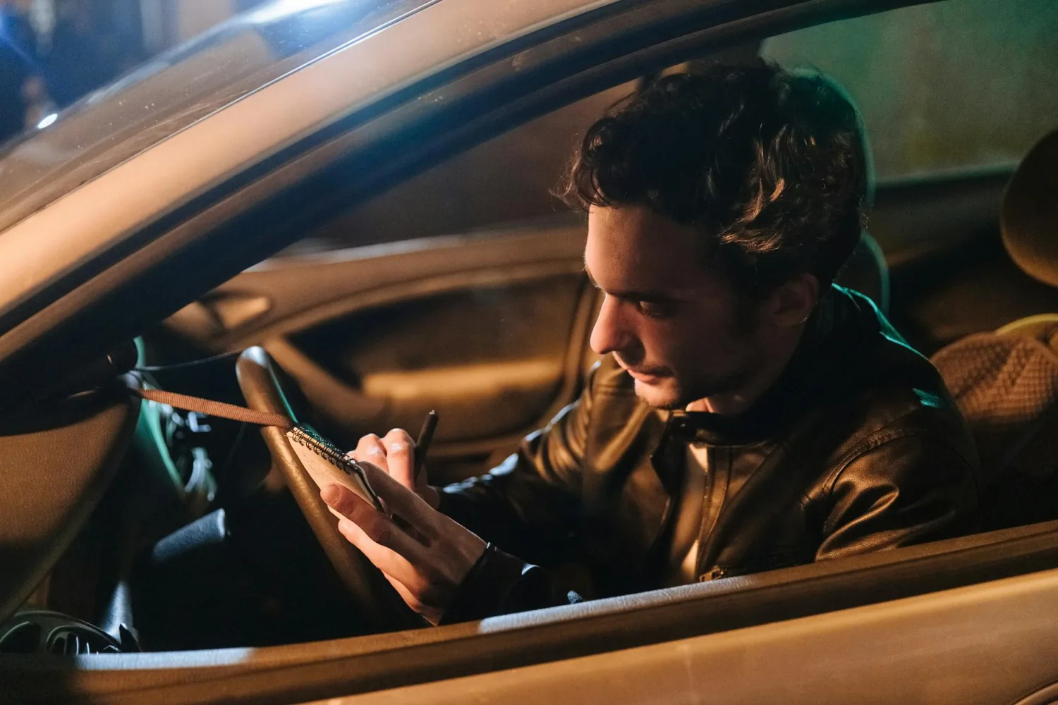 A man sitting in a car at night, writing notes in a notebook. A man sitting in a car at night, writing notes in a notebook.